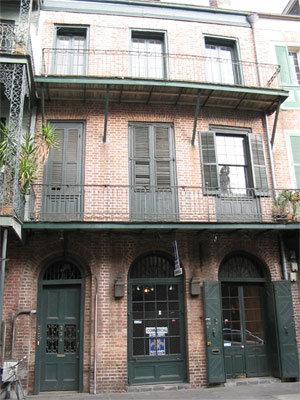 Foto da casa em New Orleans, com uma mulher olhando pela janela