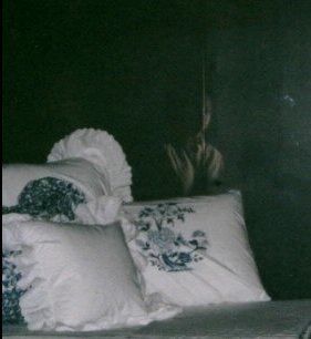 Foto de alguns travesseiros na penumbra e a imagem de uma pessoa aparece atrás deles.